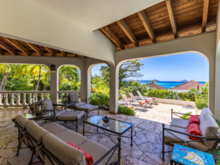 Bellamare Villa: Patio Covered stone patio with outdoor living area at Bellamare Villa with a sun deck and the water of Mahoe Bay in the background.