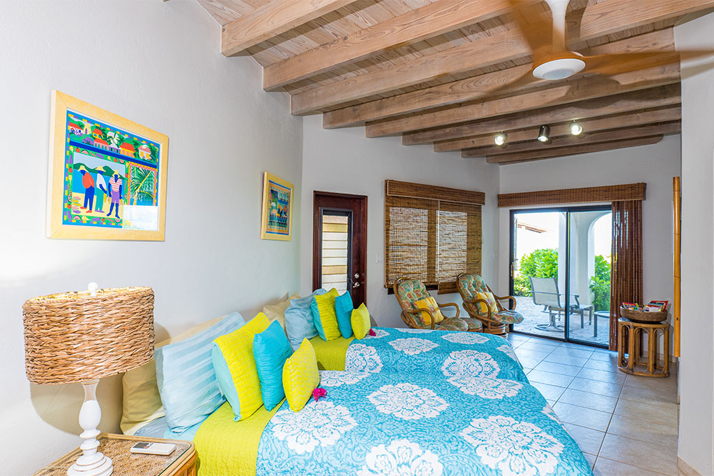 Caribbean Wind Villa twin bedroom with tile floors, a wood-beam ceiling and a sitting area with two cushioned chairs.
