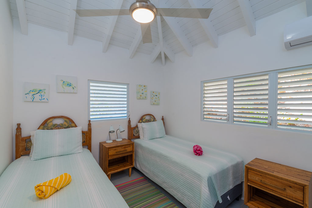 Double room with side-by-side twin beds, white walls and a vaulted ceiling with a fan.