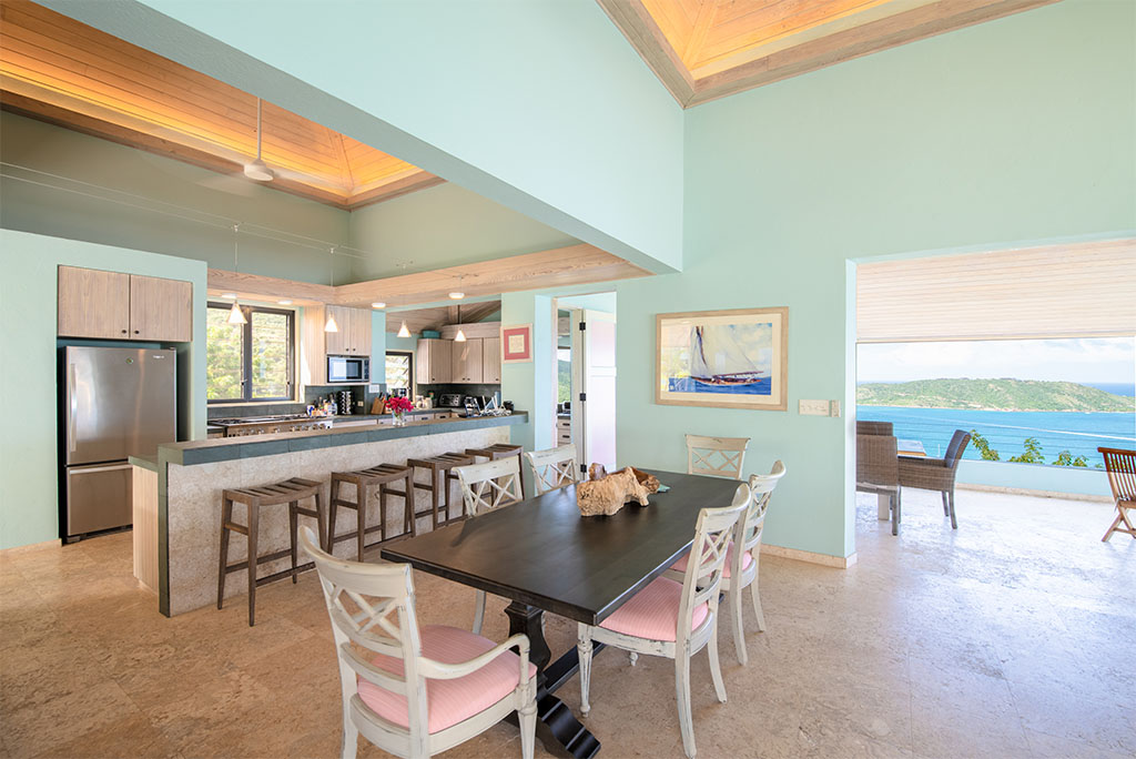 Open dining area and kitchen with stone tile floors, aqua blue walls, wood-bean ceilings and an opening to the outdoor patio.