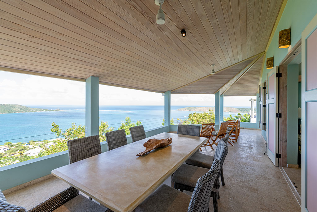 Outdoor dining table on a covered patio at Anniversary House with North Sound, Leverick Bay in the background.