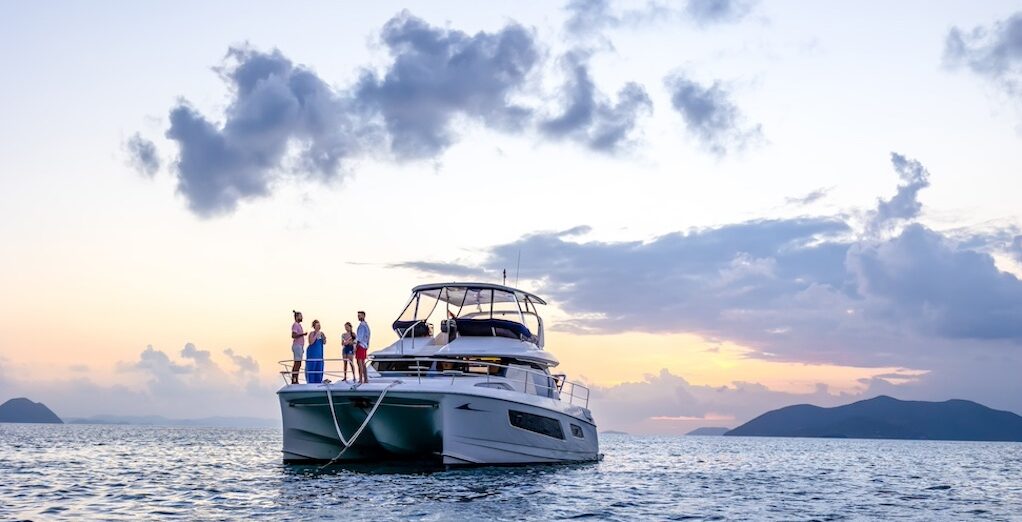 Four people stand on the deck of a pleasure boat docked in the middle of the sea with an island in the background. 