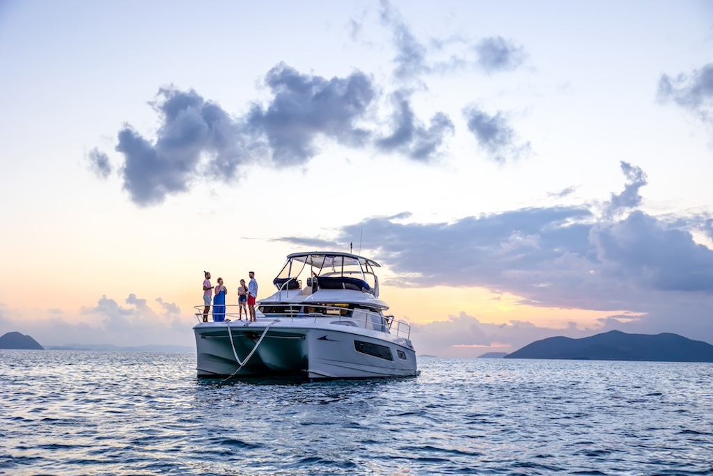 A luxury powerboat in the middle of the ocean with four people on deck standing in a circle and a dramatic sky at sunset in the background.
