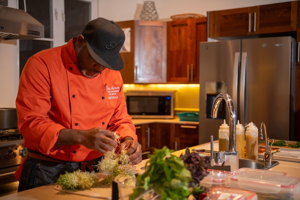 A private chef preparing food at a countertop in a villa kitchen with dark wood cabinets and steal appliances in the background.