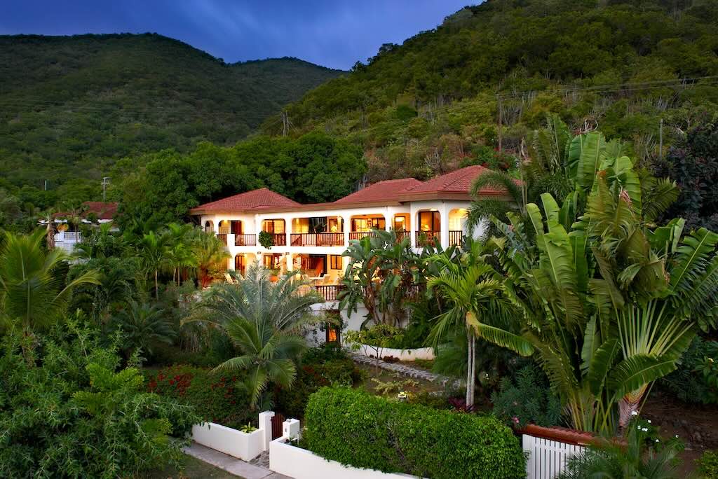 Loblolly_Exterior Loblolly Villa exterior with bright white walls, and red tiles roofs surrounded by palm trees with a green tropical hillside in the background.