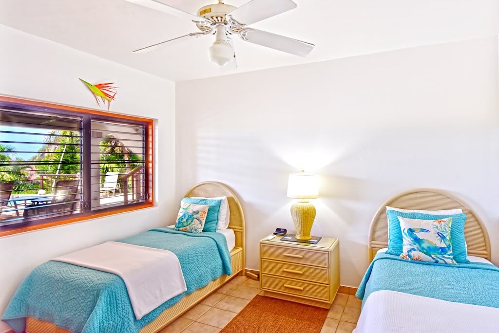 Loblolly Twin Bedroom Loblolly Villa guest room with twin beds with a table and lamp in between, a bureau, tile floors and a ceiling fan.