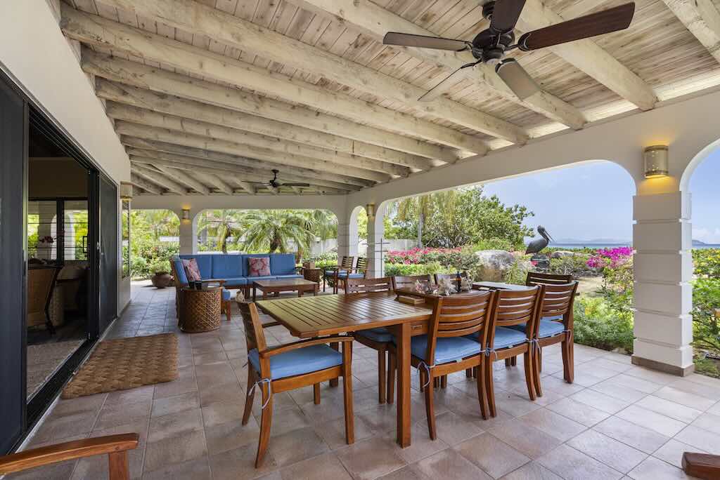 Sandcastle Villa_Covered Patio Spacious covered patio with separate dining and living areas and ceiling fans with a tropical garden and pelican sculpture in the background.