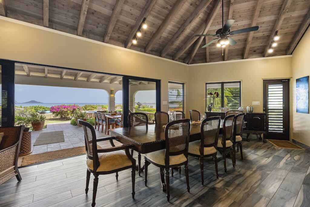 Sandcastle Villa_Dining Area Dining areas in the main room at Sandcastle Villa with an open door to the patio, garden and bay in the background.
