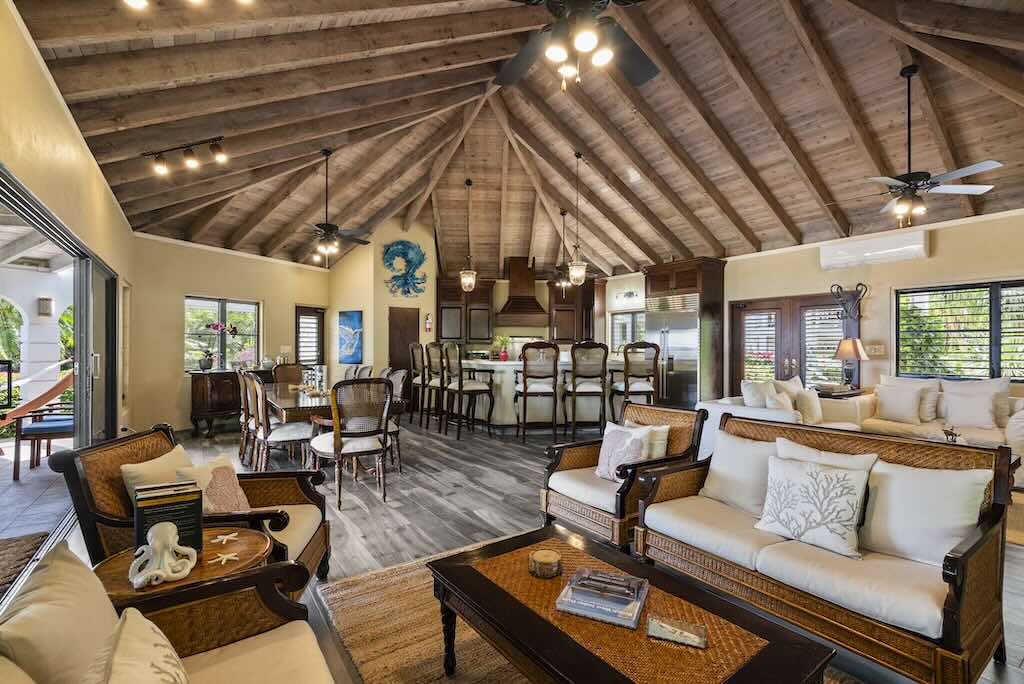 Sandcastle Villa_Great Room Great room with sitting area in the foreground and a dining table and kitchen area in the background and vaulted wood-beam ceilings.