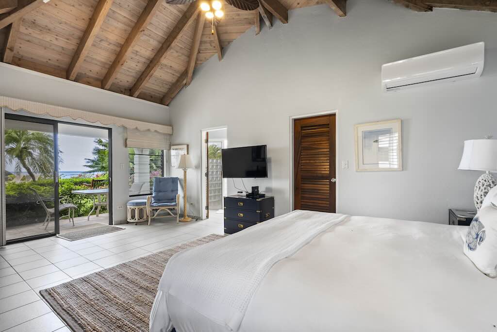 Sandcastle Villa_King Bedroom Sandcastle Villa guest room with king bed, white tile floors and a flat-screen TV mounted on the wall and an open screen door leading to a sitting area in the garden..