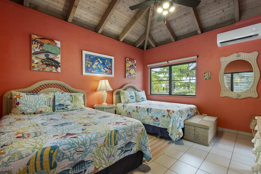 Sandcastle Villa_Double Bedroom Guest room at Sandcastle Villa with two beds, tile floors, coral colored walls and tropical art decorating the walls.